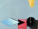 A yellow triangle, a black disc, a blue diamond, and a red square hang from wire.