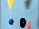 A yellow triangle, a black disc, a blue diamond, and a red square hang from wire.
