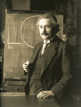 A photograph of Albert Einstein standing in front of a chalk board.