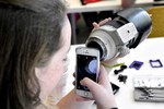 A photo of a girl using her iPhone camera to look through a telephoto lens.