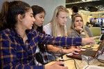 A photo of a group of girls working around a laptop.