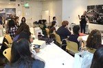 A photo of a woman standing at the front of a classroom, talking to a room full of workshop participants.